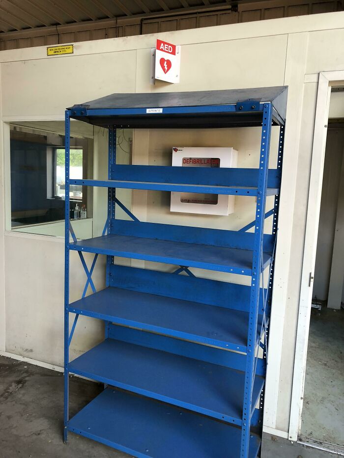 Empty blue metal shelving unit placing safety equipment out of reach in work moments demonstrating reckless safety practices.