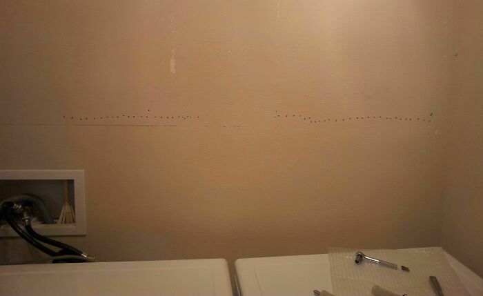 Empty wall above laundry machines with visible holes and plumbing, showing a clear DIY fail in home improvement.