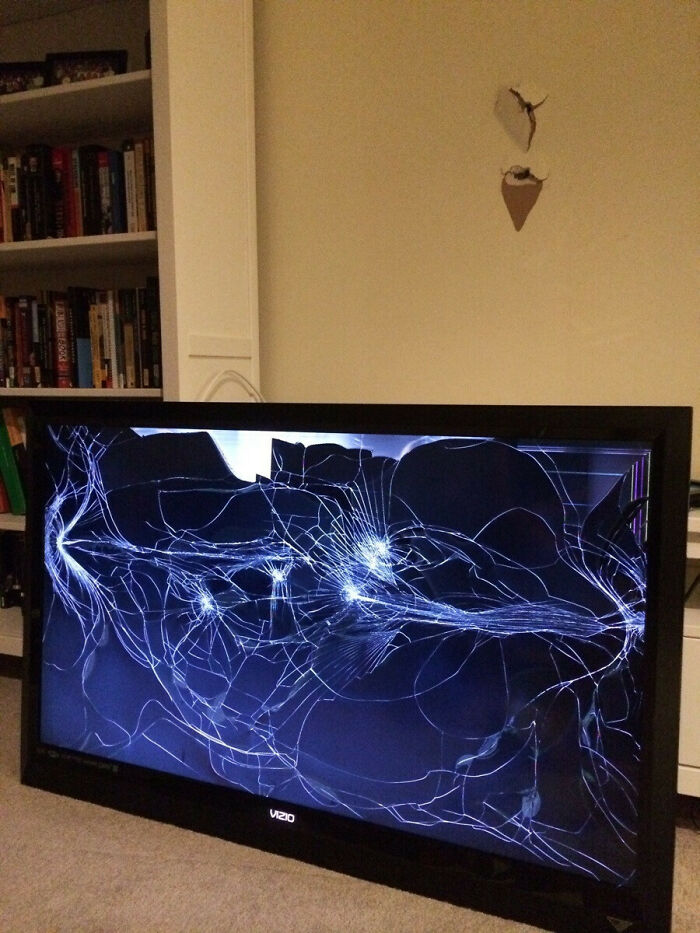 Broken Vizio TV screen with multiple spiderweb cracks showing a clear example of DIY fail and damage indoors near bookshelf.