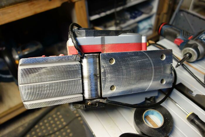 Close-up of a misaligned DIY hinge installation with visible metal parts and tools on a workbench, showing a DIY fail.