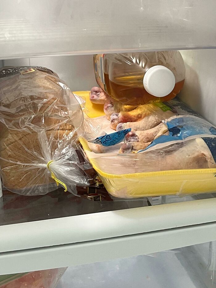 Partially frozen raw chicken legs awkwardly stored in a fridge alongside bread and a jug of liquid, roommate jerk behavior.