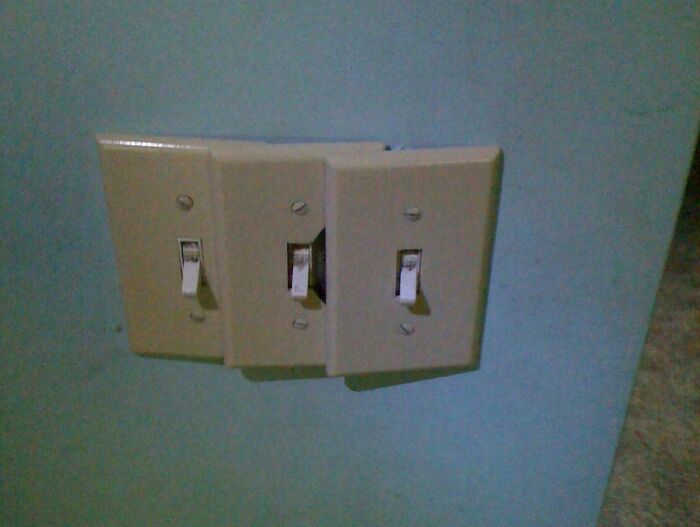 Three misaligned light switches on a blue wall showing a notable DIY fail with faulty installation.