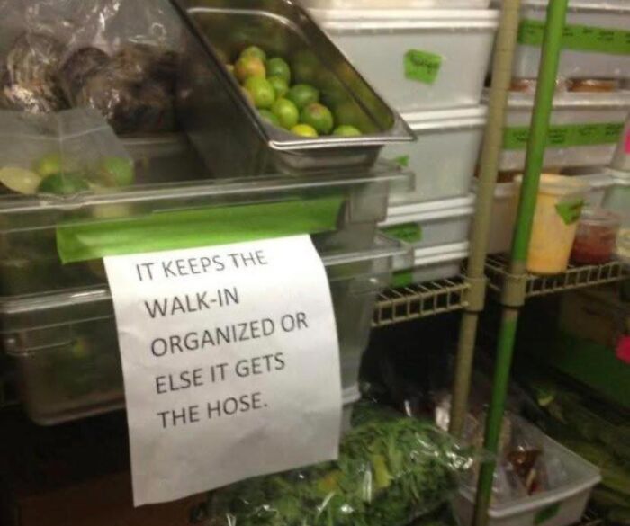 Storage area in a restaurant walk-in cooler with a humorous sign about keeping it organized for restaurant workers.