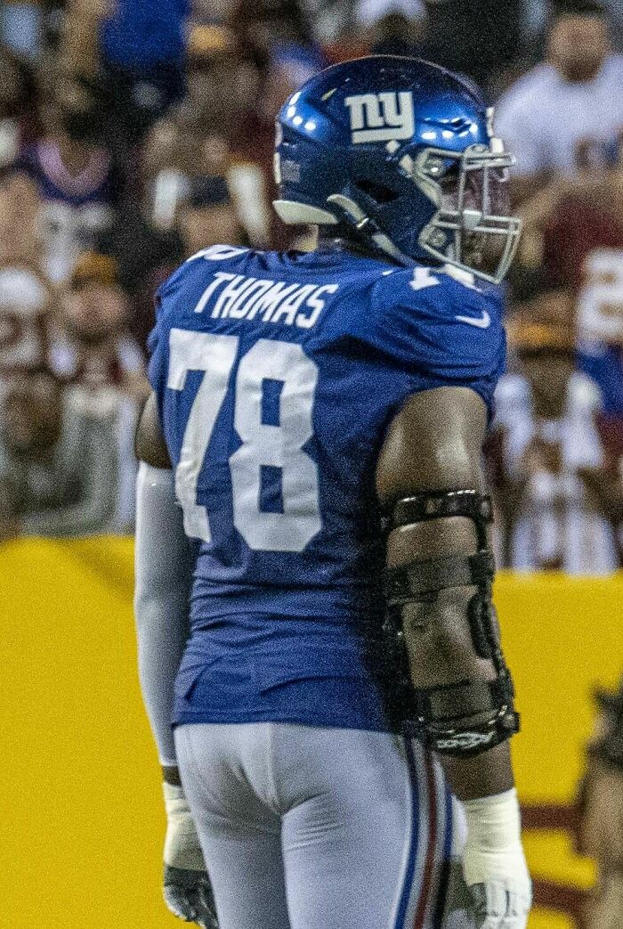 Andrew Thomas in a blue New York Giants uniform with helmet and protective gear on the football field during a game.