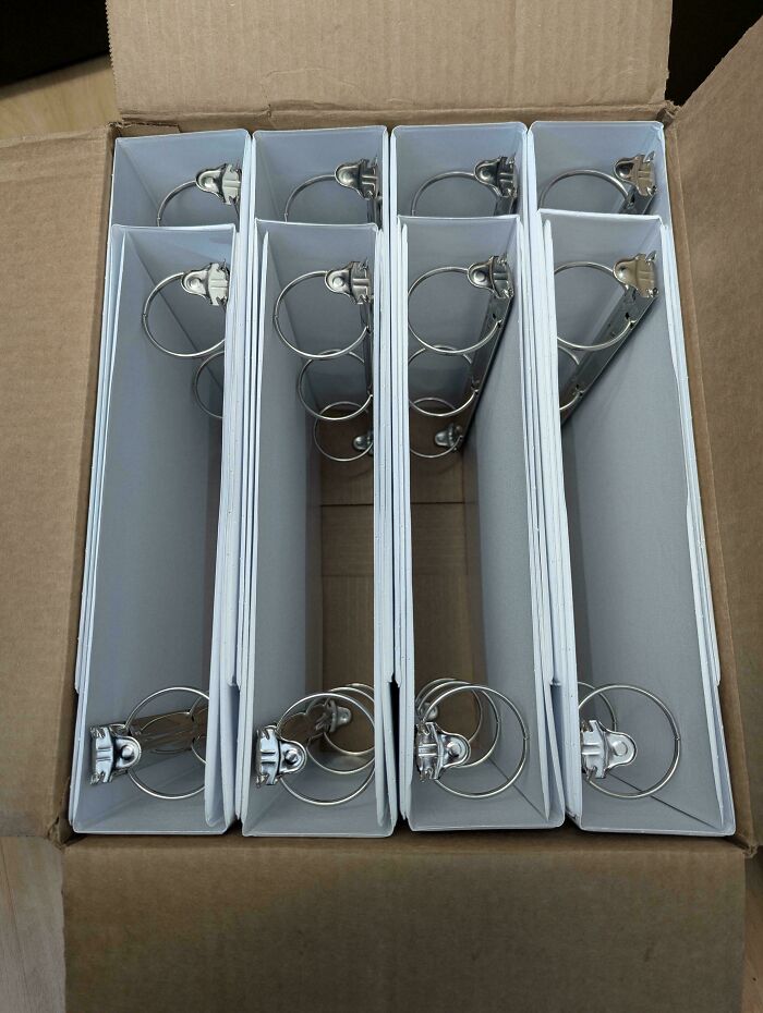 Five white metal ring binders neatly organized and aligned inside a cardboard box for efficient storage.