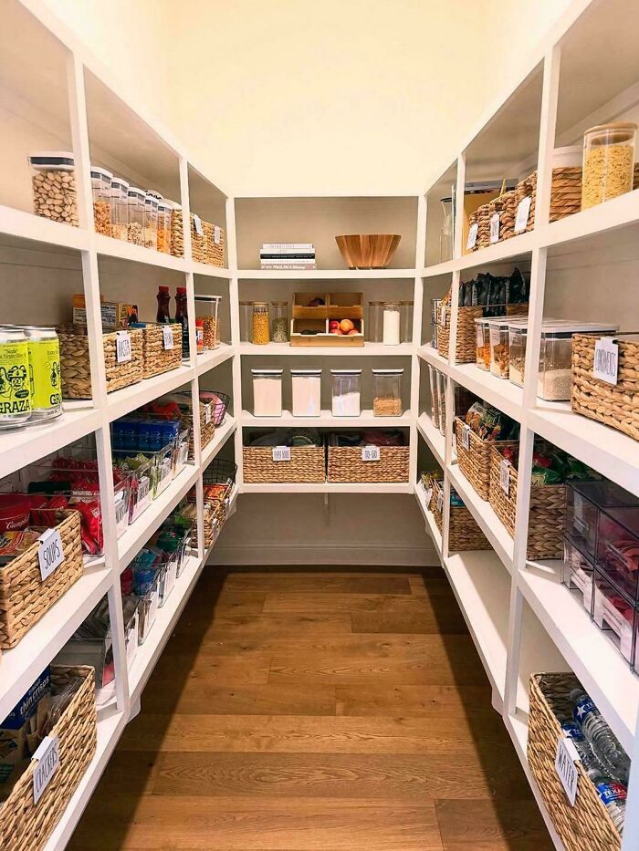 Pantry with neatly organized food items and baskets on white shelves showcasing satisfying organization and order.