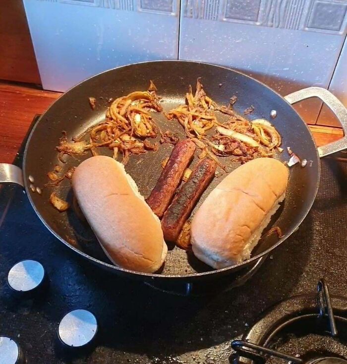 Burnt sausages and overheated onions in a pan with two buns, showing jerks that made roommates want to live alone.
