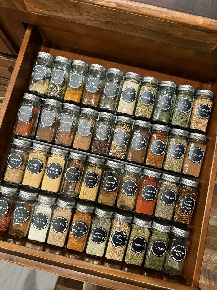 Neatly organized spice jars with clear labels arranged in a drawer, showcasing a satisfying and orderly kitchen setup.