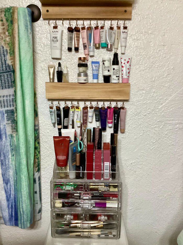 Neatly organized makeup and skincare products displayed with hanging clips and clear acrylic drawers for easy access and order.