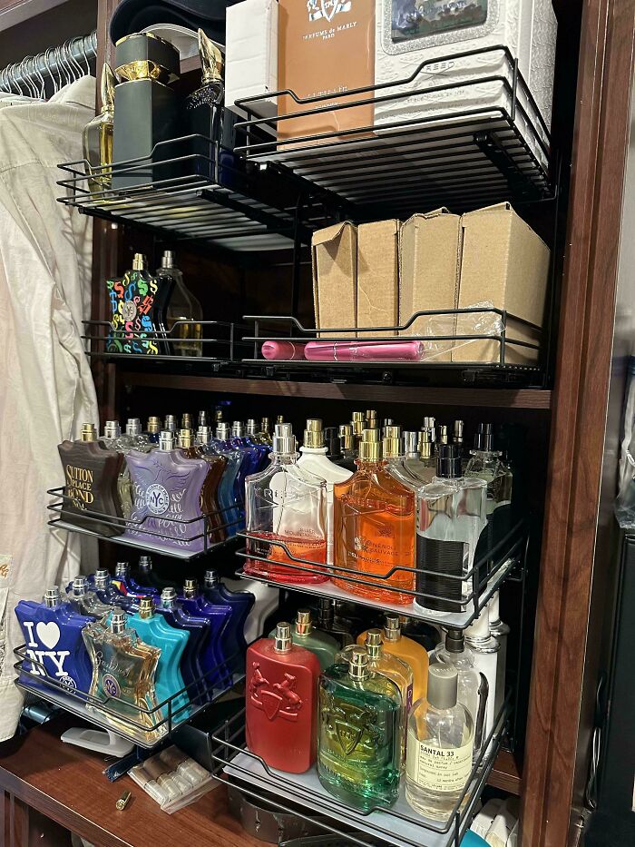 Neatly organized perfume bottles and boxes arranged on metal shelves inside a wooden closet for a tidy display.