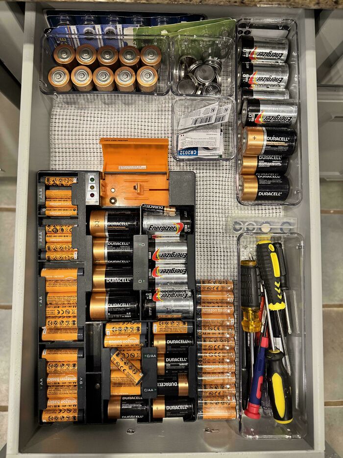 Drawer neatly organized with various batteries sorted by type and size alongside screwdrivers and small tools arranged clearly