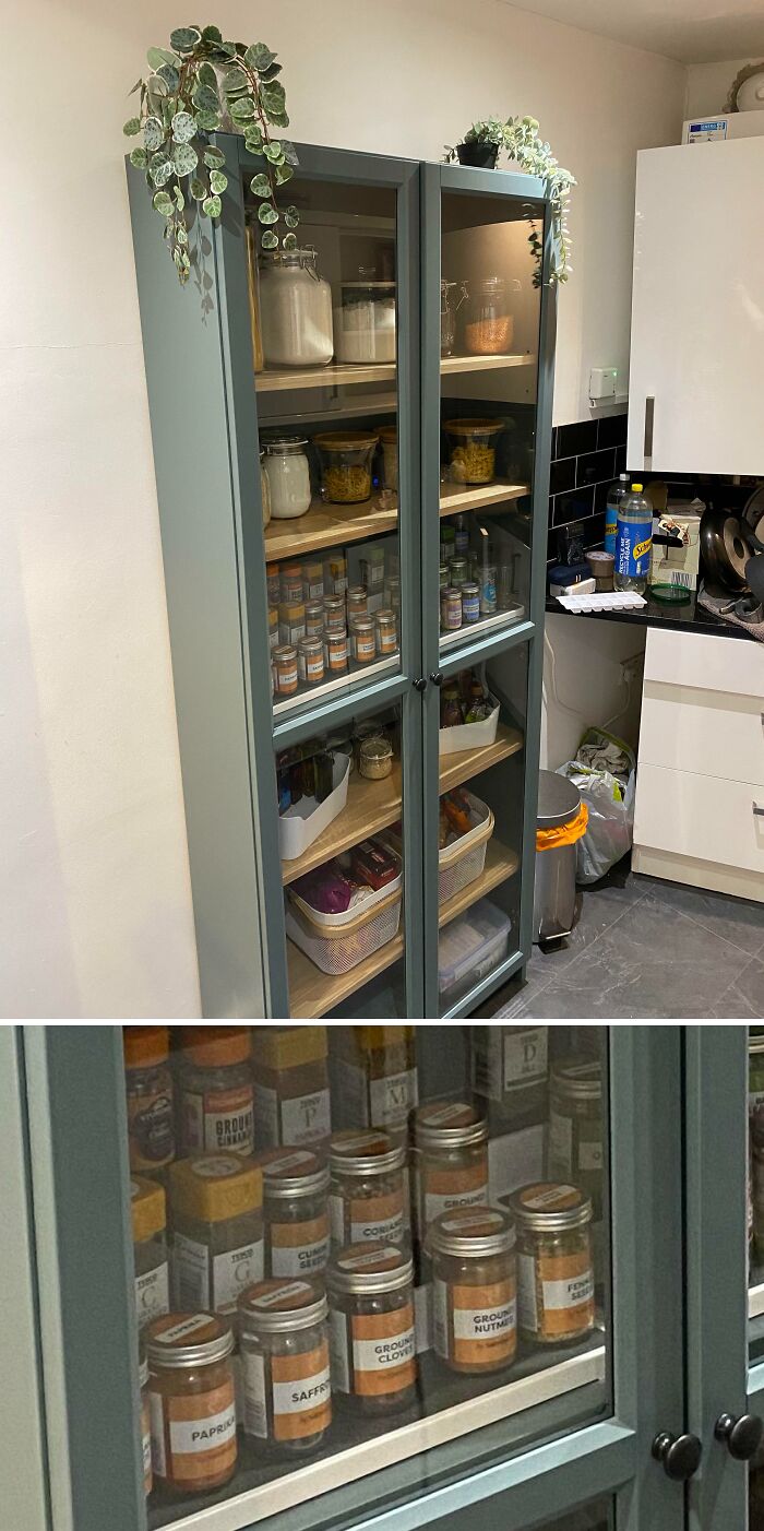 Neatly organized kitchen pantry cabinet with labeled spice jars and neatly arranged food containers behind glass doors.