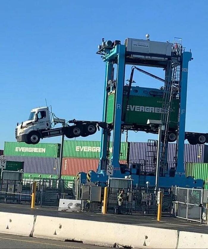 Reckless work moment showing a truck dangerously lifted by a shipping container crane at a busy cargo terminal.