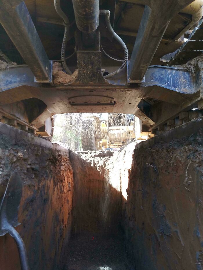 Heavy machinery pouring dirt into a deep trench at a construction site, illustrating reckless work moments in safety.