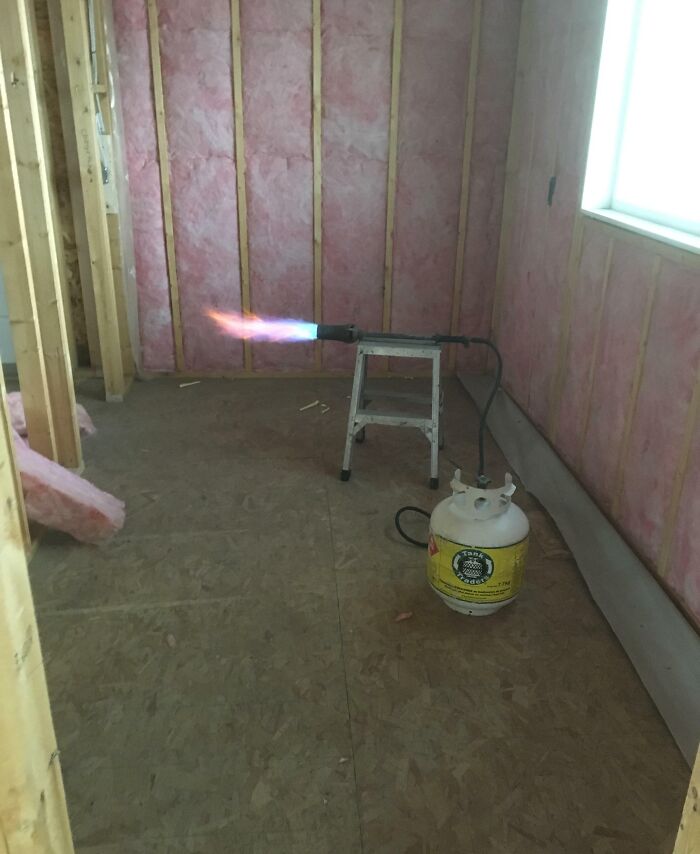 Propane torch left unattended on a step ladder inside an unfinished room with exposed insulation, showing reckless work moment.