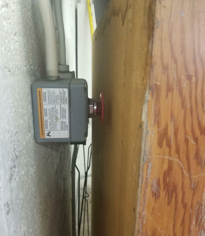 Emergency stop button mounted dangerously close to a wooden surface, illustrating reckless work moments in safety hazard scenarios.