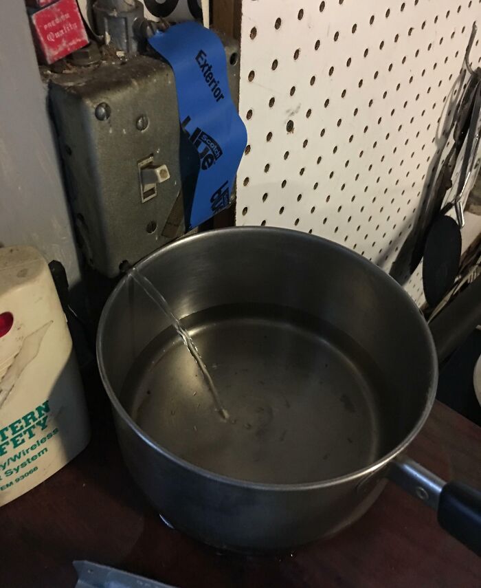 Reckless work moment with water pouring into a metal pot near an exposed electrical switch on a cluttered workbench.