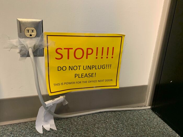 Power cord taped to outlet with bright warning sign highlighting reckless work moment in need of safety awareness.
