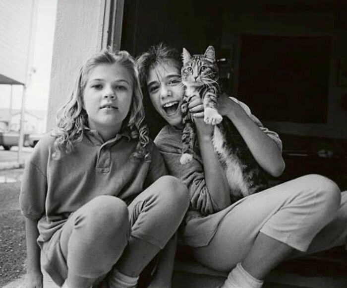 Two children sitting together with a cat, showcasing timeless feline charm in this vintage photo from history.