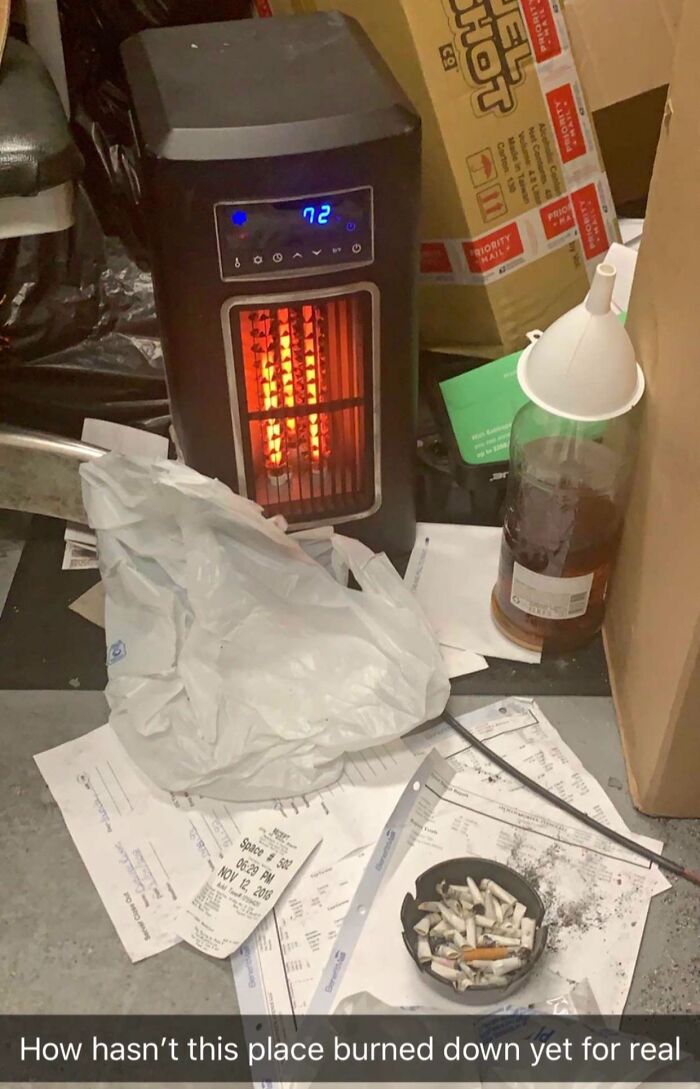 Reckless work moment with heater near papers and cigarette butts creating a serious fire hazard in a cluttered workspace.