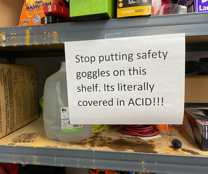 Warning sign on an acid-covered shelf telling workers not to put safety goggles there in a reckless work moment.