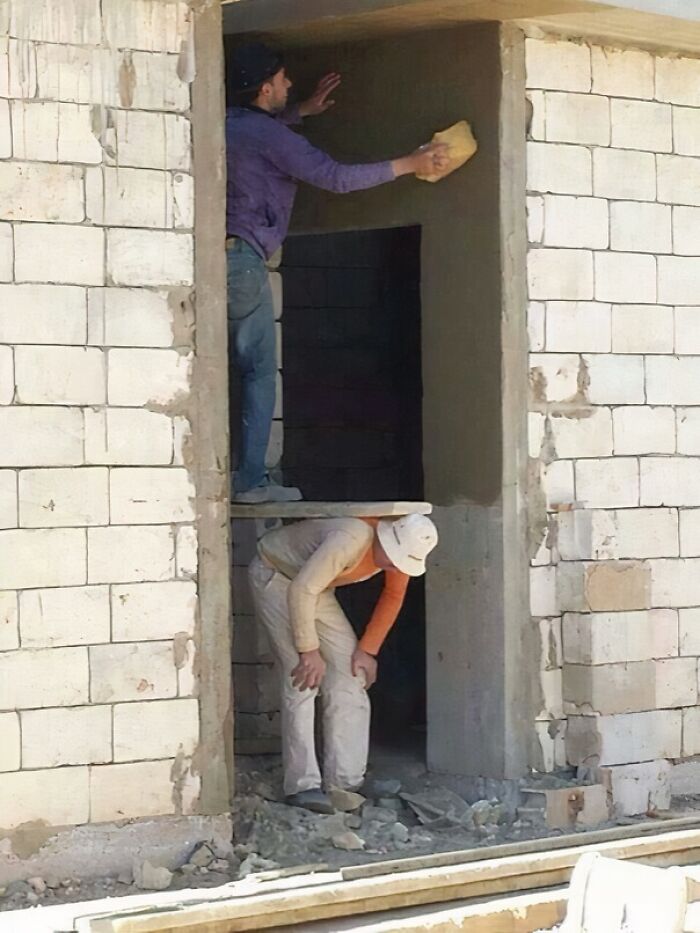 Two construction workers showing reckless work moments, one standing on a narrow plank above the other without safety gear.