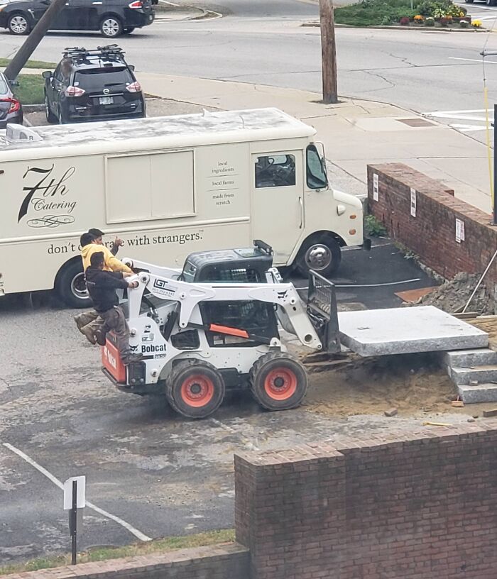 Two men riding dangerously on the back of a Bobcat loader at a construction site, showcasing reckless work moments.