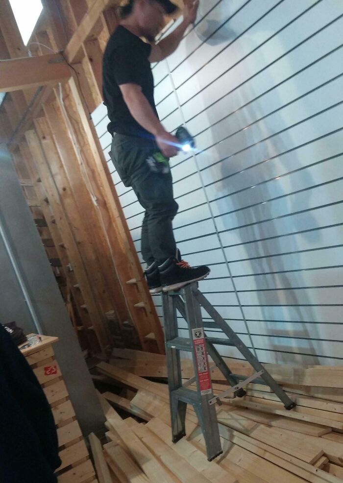 Man standing recklessly on top of a ladder in a cluttered work area showing unsafe work moments for safety videos.