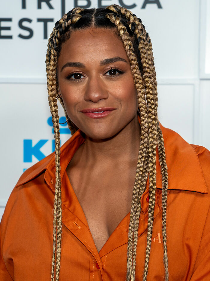 Ariana DeBose with braided hair and an orange shirt smiling at a Tribeca event, highlighting her bio and career.