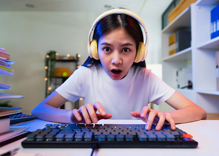 Young woman with headphones typing on keyboard, expressing surprise while discussing overused slang words to be banished in 2026. Young woman with headphones typing on keyboard, expressing surprise while discussing overused slang words to be banished in 2026.