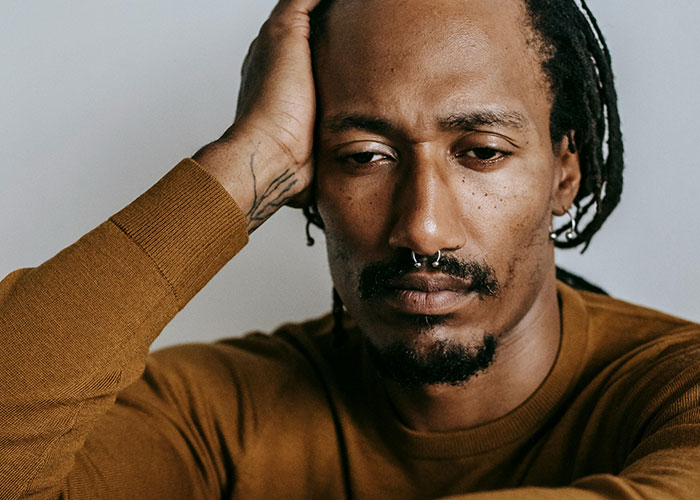 Man with septum piercing and dreadlocks looking thoughtful and distressed, reflecting on discovering he is not the biological parent.