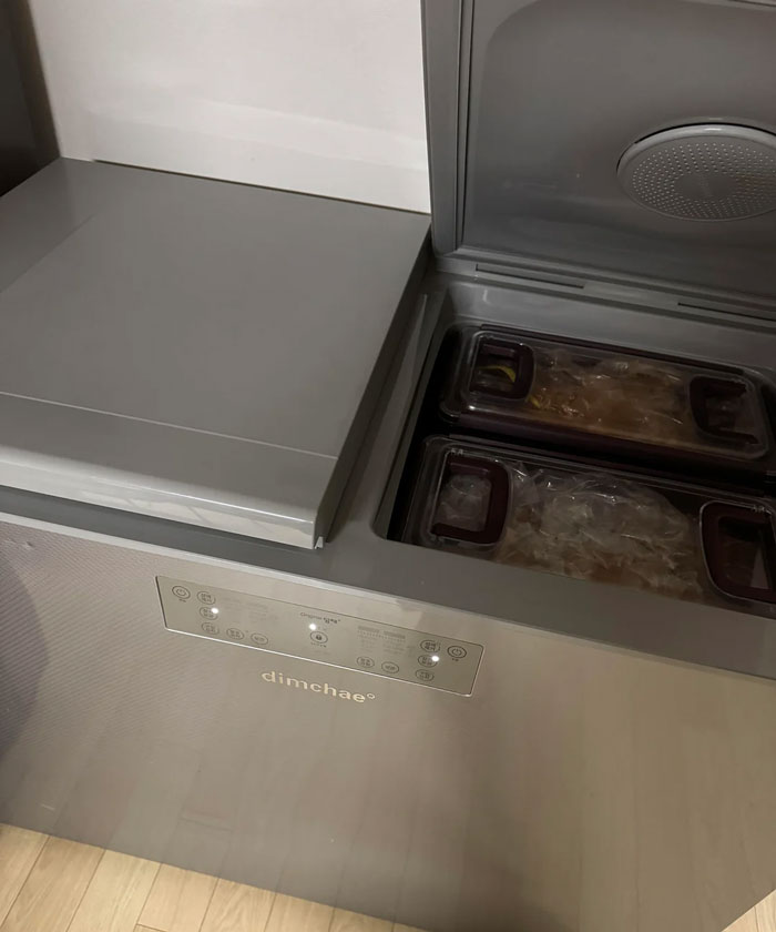 Gray dimchae Korean household item freezer chest open with plastic containers inside on wooden floor