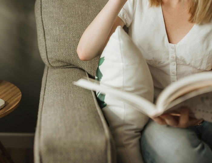 Person reading a book on a couch, demonstrating smart thinking in a cozy home environment.