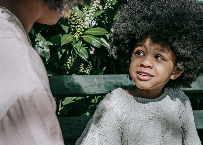 Child with no filter sharing family lore outdoors on a sunny day, sitting on a bench talking to an adult.