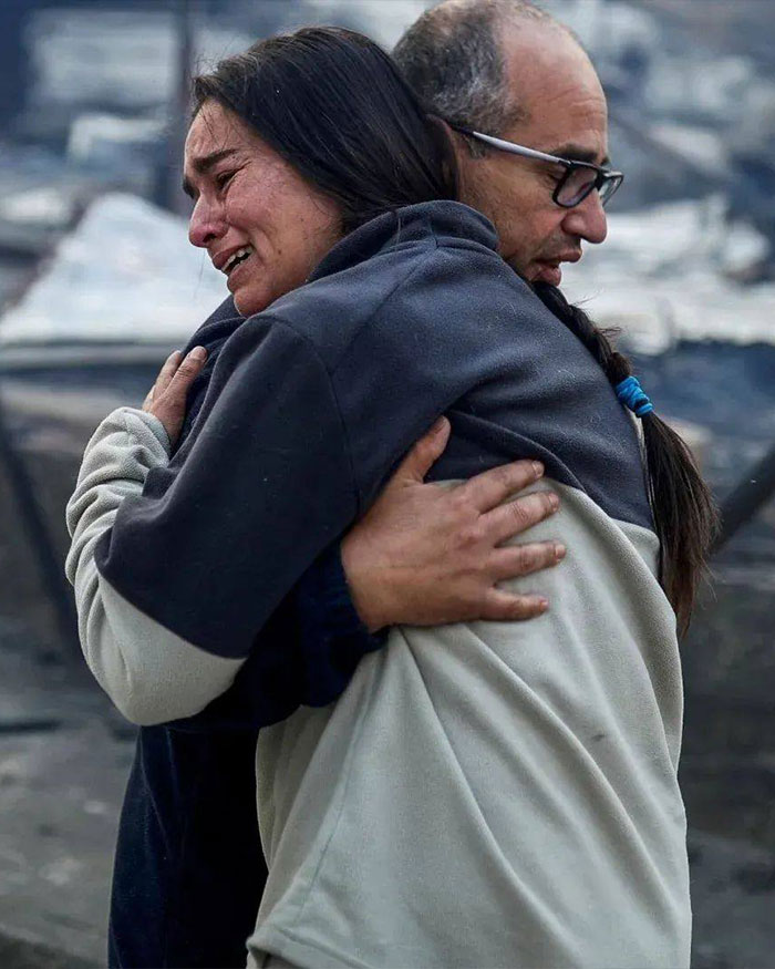 Two volunteers embracing amid chaos after Chile wildfires burned town overnight, showing emotional distress and support.