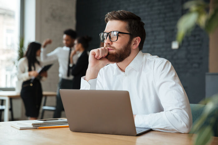 Young man wearing glasses looking thoughtful at laptop, reflecting on moments that hit people harder than expected.
