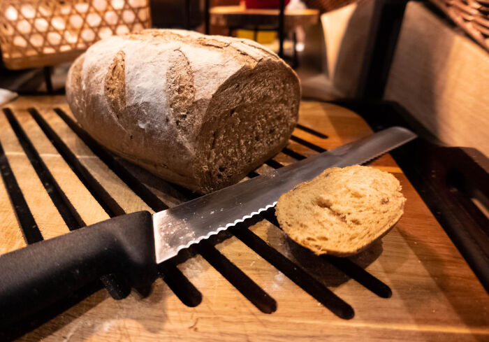 A loaf of bread with a slice cut next to a knife on a wooden cutting board, illustrating weird iconic satisfying situations.