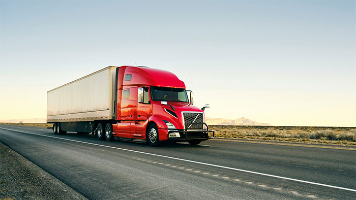 Red semi truck driving on an empty highway in a desert landscape under a clear sky.