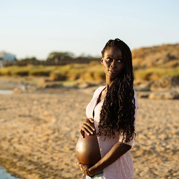 Pregnant woman on a beach at golden hour, holding her belly in a creative maternity photoshoot ideas pose.