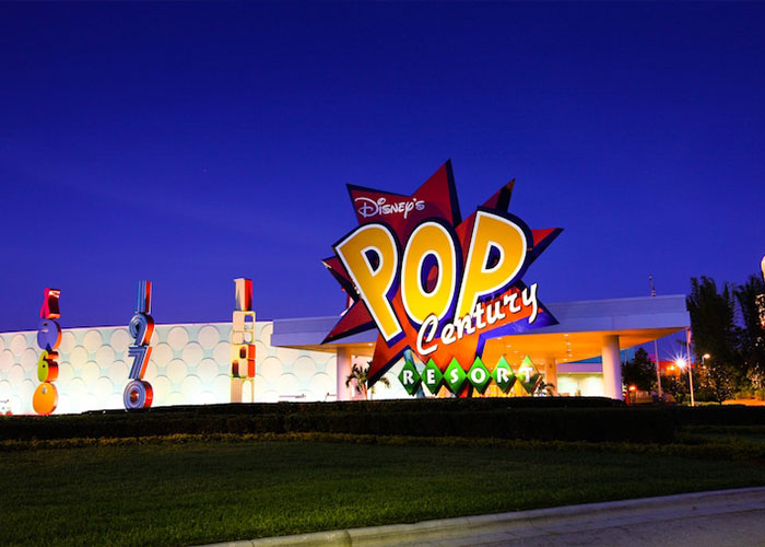 Pop Century Resort entrance sign illuminated at night at Disney World, colorful retro signage and resort driveway Pop Century Resort entrance sign illuminated at night at Disney World, colorful retro signage and resort driveway