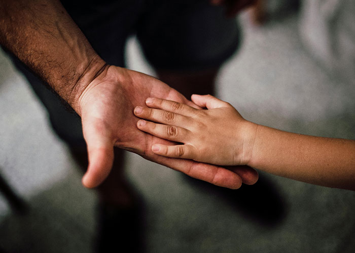 Adult man's hand holding a child's hand symbolizing connection and emotions of not being the biological parent.