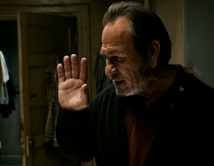 Older man raising hand indoors, illustrating movie set workers sharing stories about biggest diva stars they've worked with.