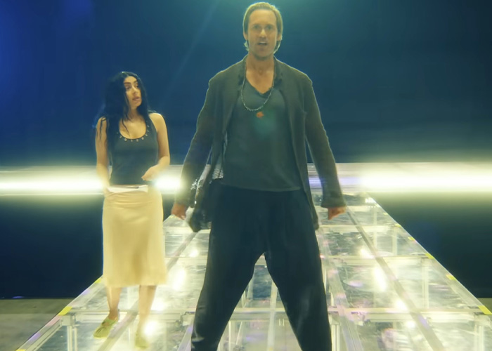 Two individuals on a brightly lit platform in a dark setting, with a focus on Charli XCX style and edgy fashion.