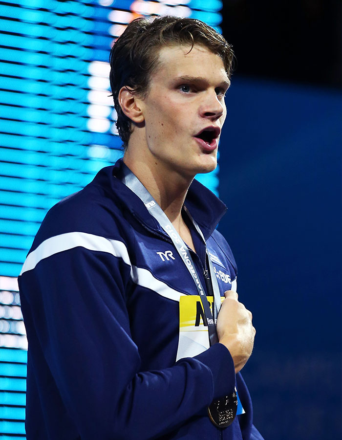 Young Olympic gold medalist in a navy tracksuit with medal around neck, expressing emotion during a sports event.