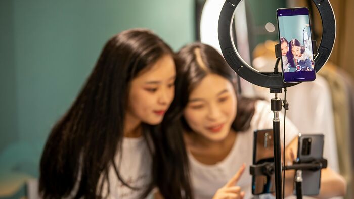 Two women recording a video with a smartphone and ring light, engaging viewers to cast their vote on the right thing.