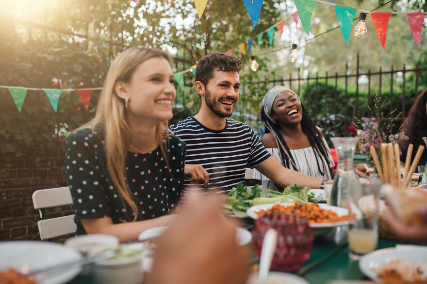 Friends laughing and having fun outdoors during a meal, enjoying paranoia questions to get secrets spilled.