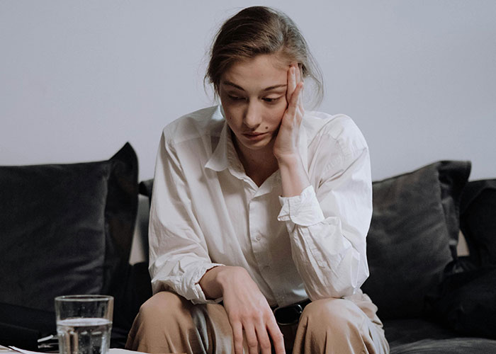 Young woman in a white shirt sitting on a couch looking thoughtful, reflecting on neurodivergent experiences.