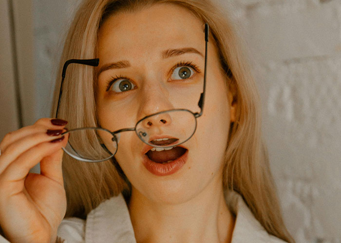 Young woman holding glasses with surprised expression illustrating kids with no filter revealing family lore moments.