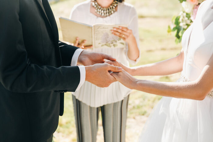 Bride and groom holding hands during wedding ceremony with officiant reading vows, capturing candid wedding moments.