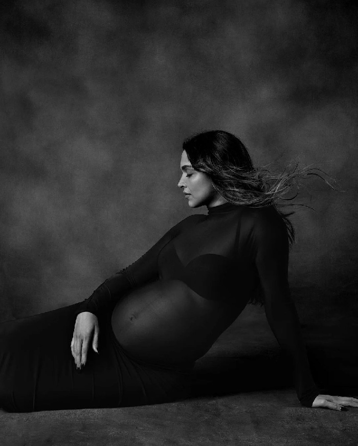 Pregnant woman reclining in black sheer gown, side profile with flowing hair, elegant studio maternity photoshoot ideas